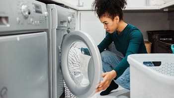 vrouw zit gehurkt voor wasmachine om deze te schoonmaken